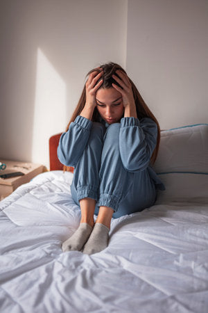 Mulher de pijama sentada na cama com a cabeça entre as mãos