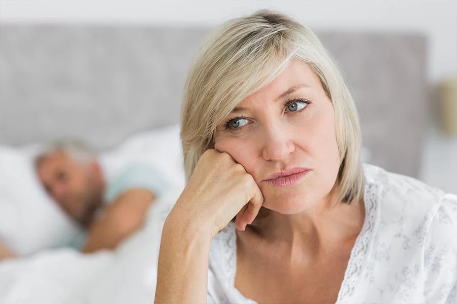 Mulher acordada na cama, de costas para o marido que dorme